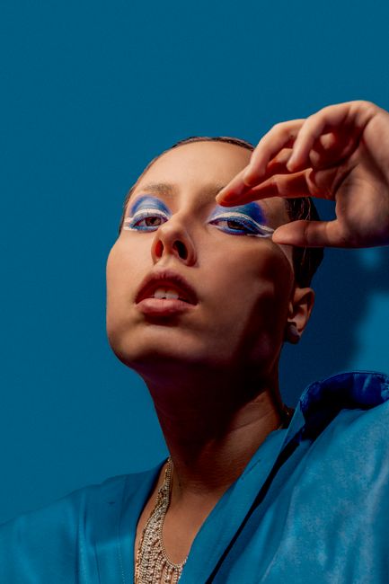 Striking fashion portrait of a woman with bold blue makeup against a vibrant background.