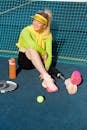 Woman in Green Long Sleeve Shirt and Black Pants Sitting on Tennis Court