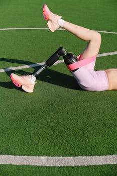 An athlete with a prosthetic leg stretching on a football pitch, focusing on adaptive fitness and sports clothing.