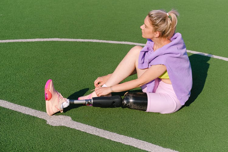 Woman With Prosthetic Leg Tying Shoe On Sports Field