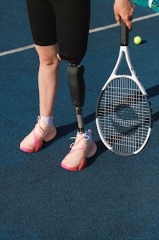 Athlete with prosthetic leg standing on tennis court, holding a racket, ready to play.