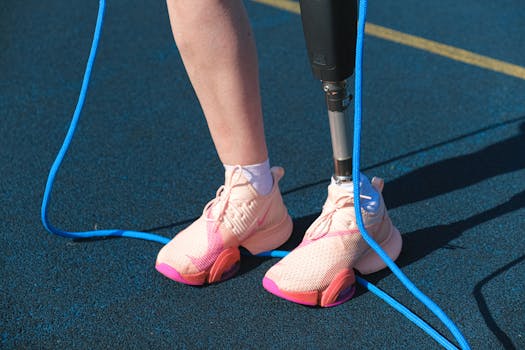 Close-up of an athlete with a prosthetic leg tying pink running shoes on a track.
