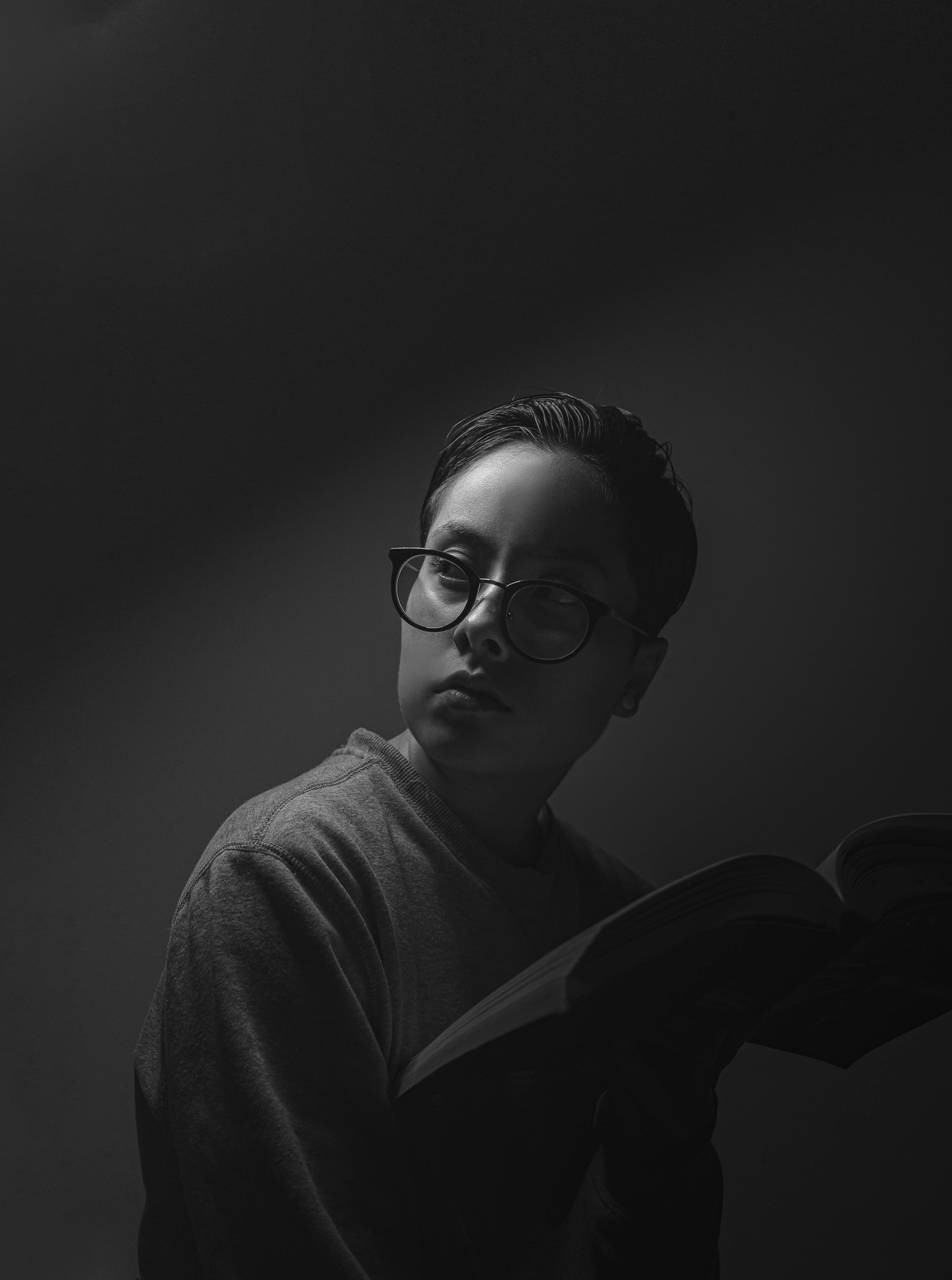Dramatic black and white portrait of a person reading with glasses.