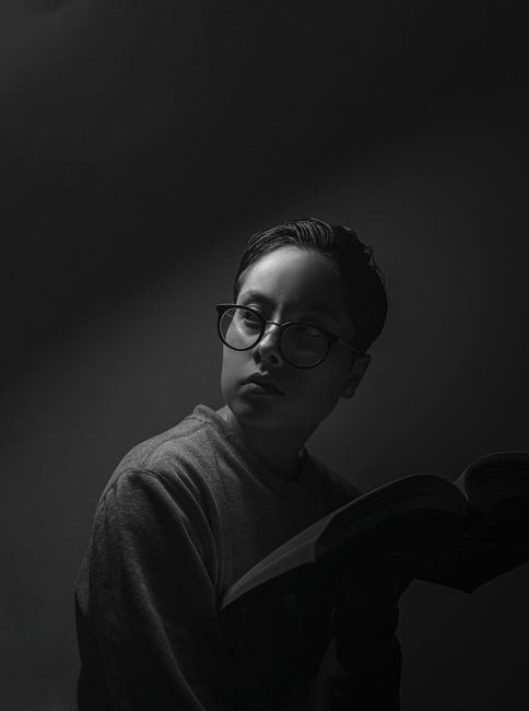 Dramatic black and white portrait of a person reading with glasses.