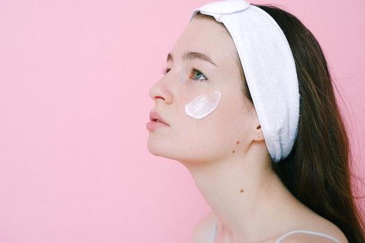 一位安详的女人在粉色背景下往脸颊上涂抹护肤霜