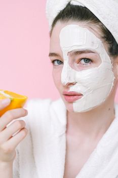 一位年轻女子头裹面膜和毛巾，手拿橘子，正在推销护肤品