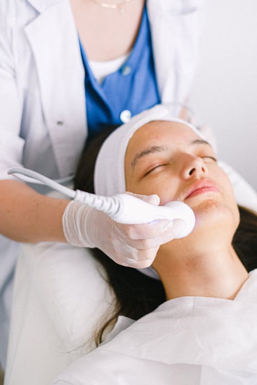 Free Beautician doing ultrasonic face cleaning for young client Stock Photo