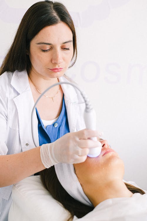 Concentrated cosmetologist treating clients face skin with ultrasonic apparatus