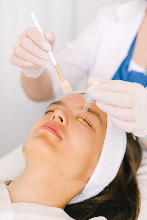 Free Cosmetologist applying essential oil on client face Stock Photo