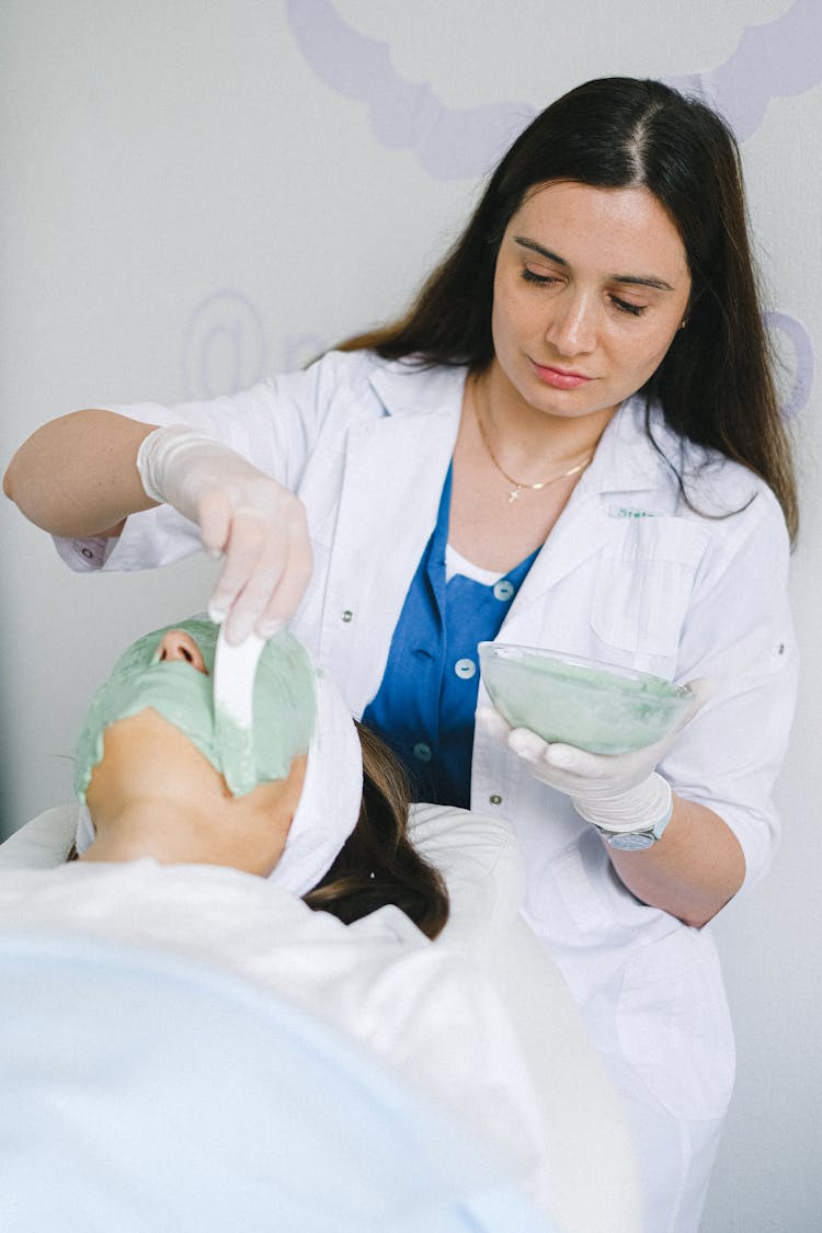 Focused Cosmetologist Applying Mask On Female Client