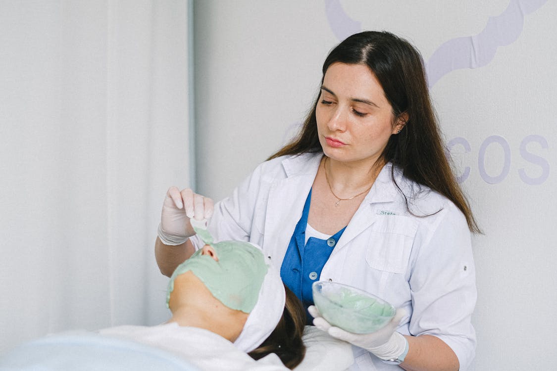 Woman getting facial nourishing mask by beautician at spa salon