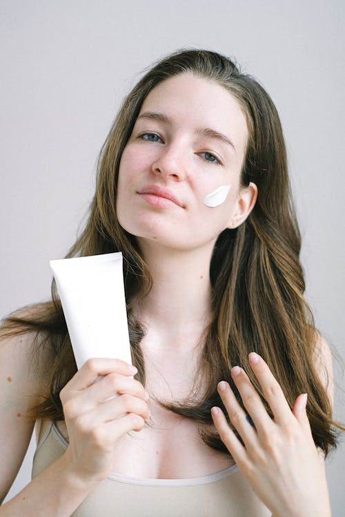 Confident young lady demonstrating cosmetic product while looking at camera with white swear on face on white background
