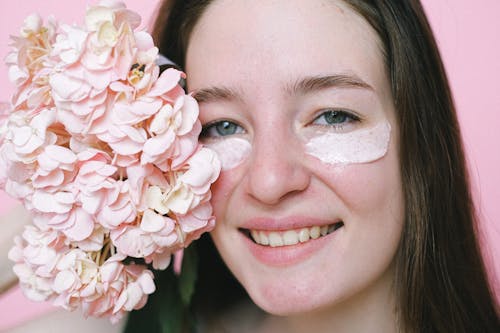 Free Crop positive young female model with eyes mask smiling at camera while demonstrating hydrangea flower on pink background Stock Photo