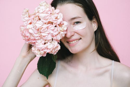 Free Smiling woman covering eye with pink flower while standing against pink background Stock Photo