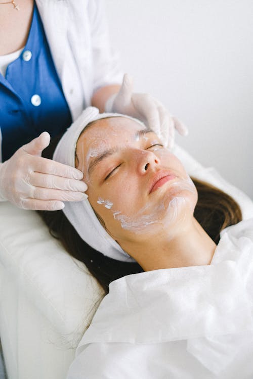 Free Crop beautician massaging client face with lotion during spa procedures Stock Photo