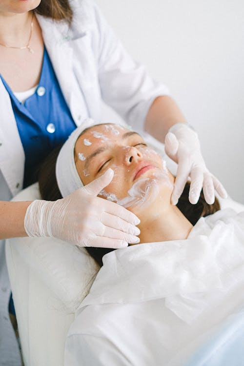 Free From above of crop faceless cosmetician applying facial mask on customer face during cosmetic procedure in modern spa salon Stock Photo