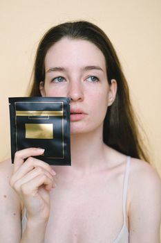 Calm model with brown hair in top showing facial mask and looking away against light background in studio
