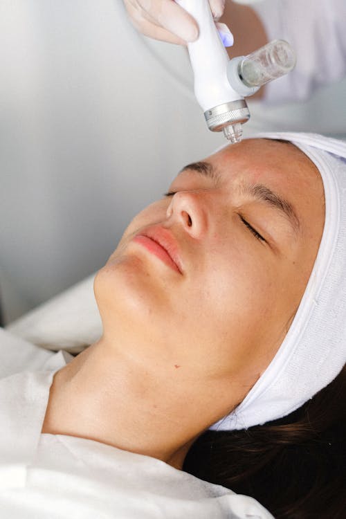 High angle of crop professional cosmetician doing face skin care therapy with laser tool