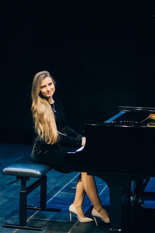 Woman in Black Long Sleeve Dress Sitting in front of a Grand Piano