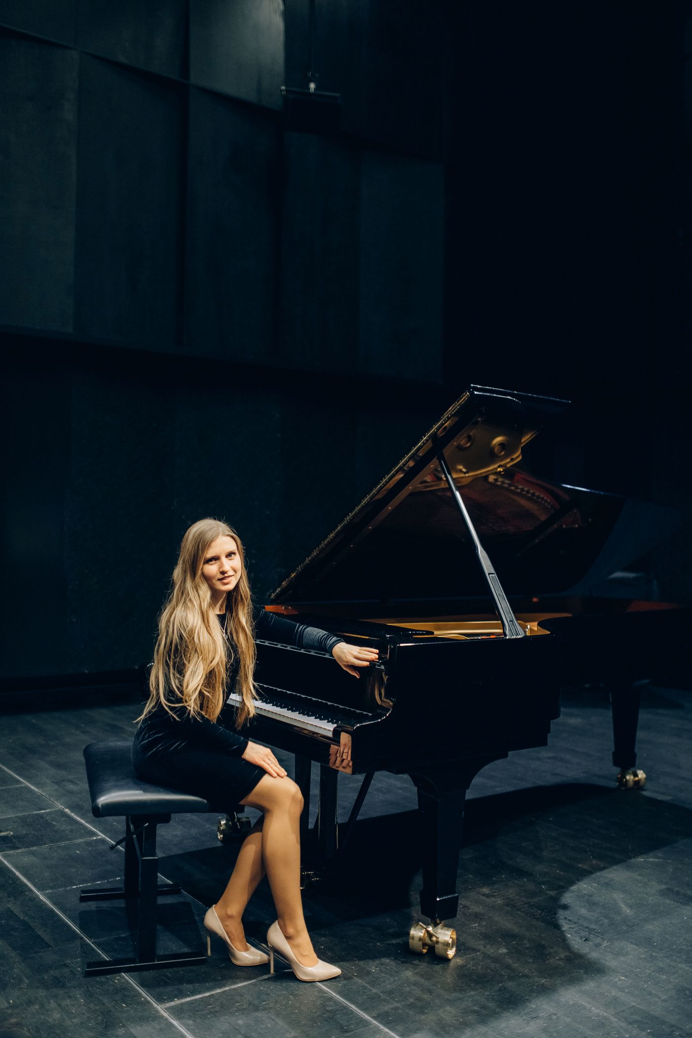 A concert pianist seated beside a grand piano
