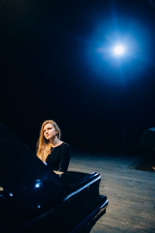 Free A woman in black long sleeves sits at a grand piano under a bright spotlight, exuding elegance and focus. Stock Photo