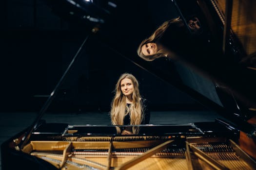A young woman is seated at a grand piano on a dimly lit stage, captured in an artistic profile.