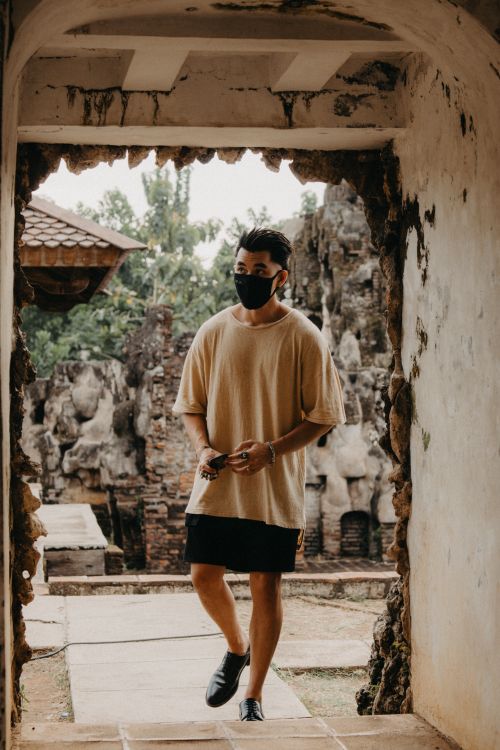 Free Man with face mask stands in ancient stone archway amidst a historic backdrop, symbolizing new normal. Stock Photo