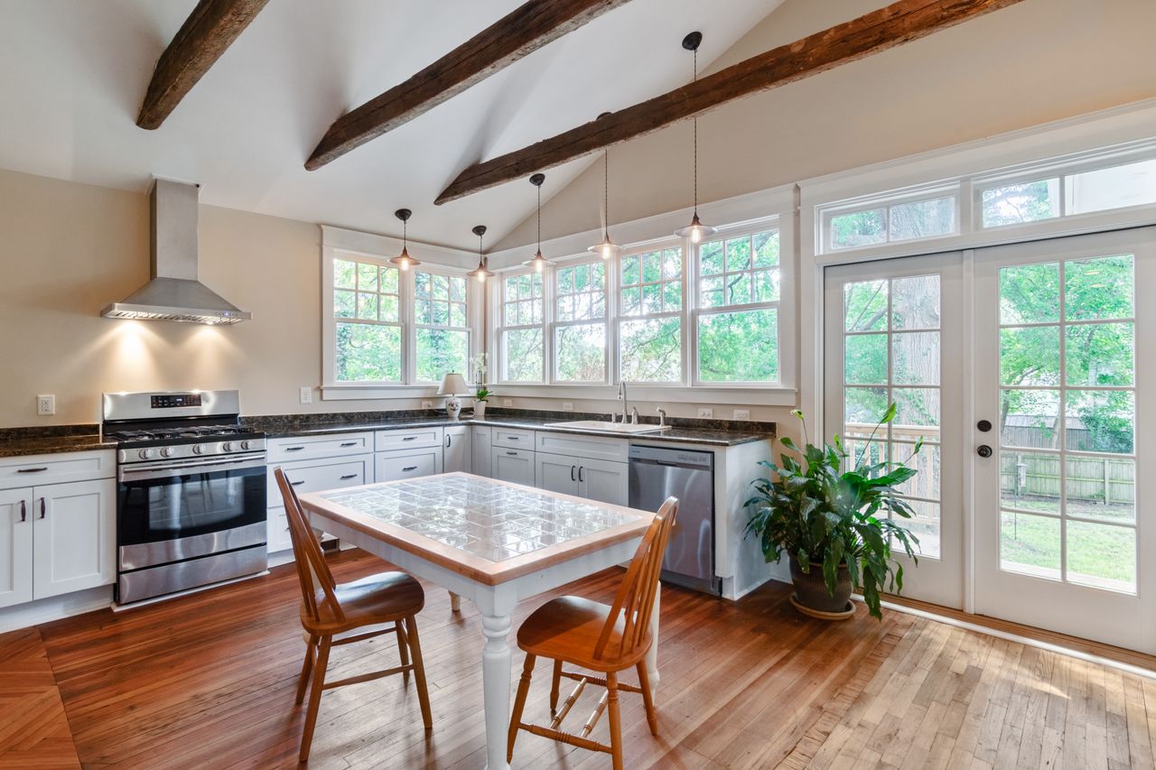Bright farmhouse kitchen with heavy rustic wood ceiling beams, pendant lights and a wooden dining table