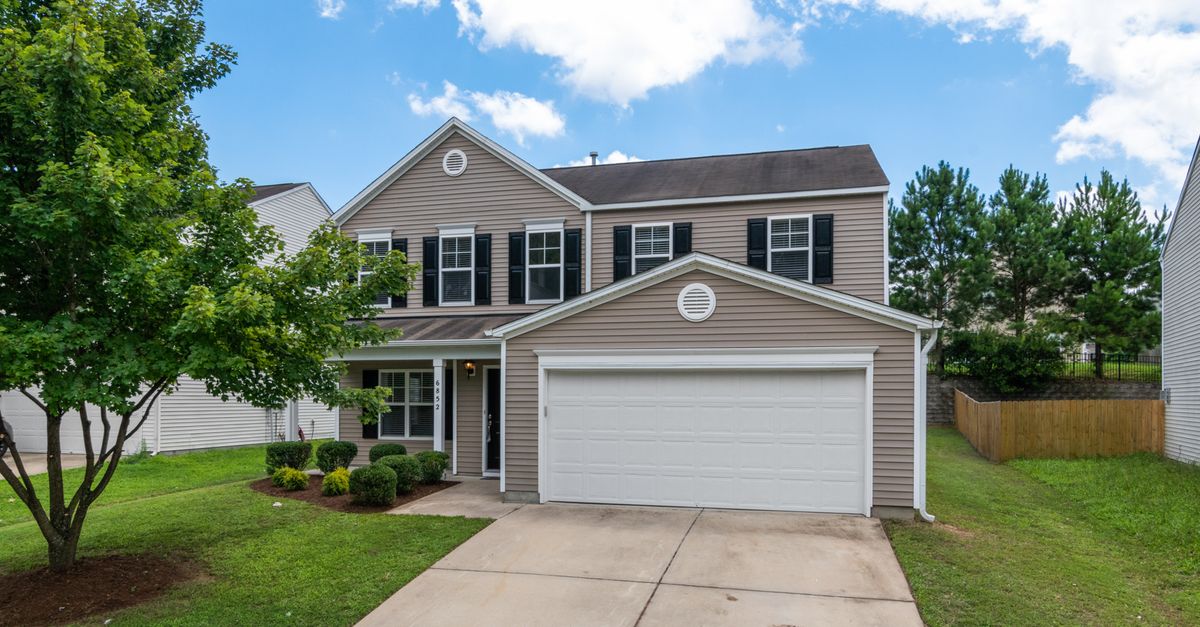 Charming two-story suburban home with green lawn, two-car garage, and blue sky.