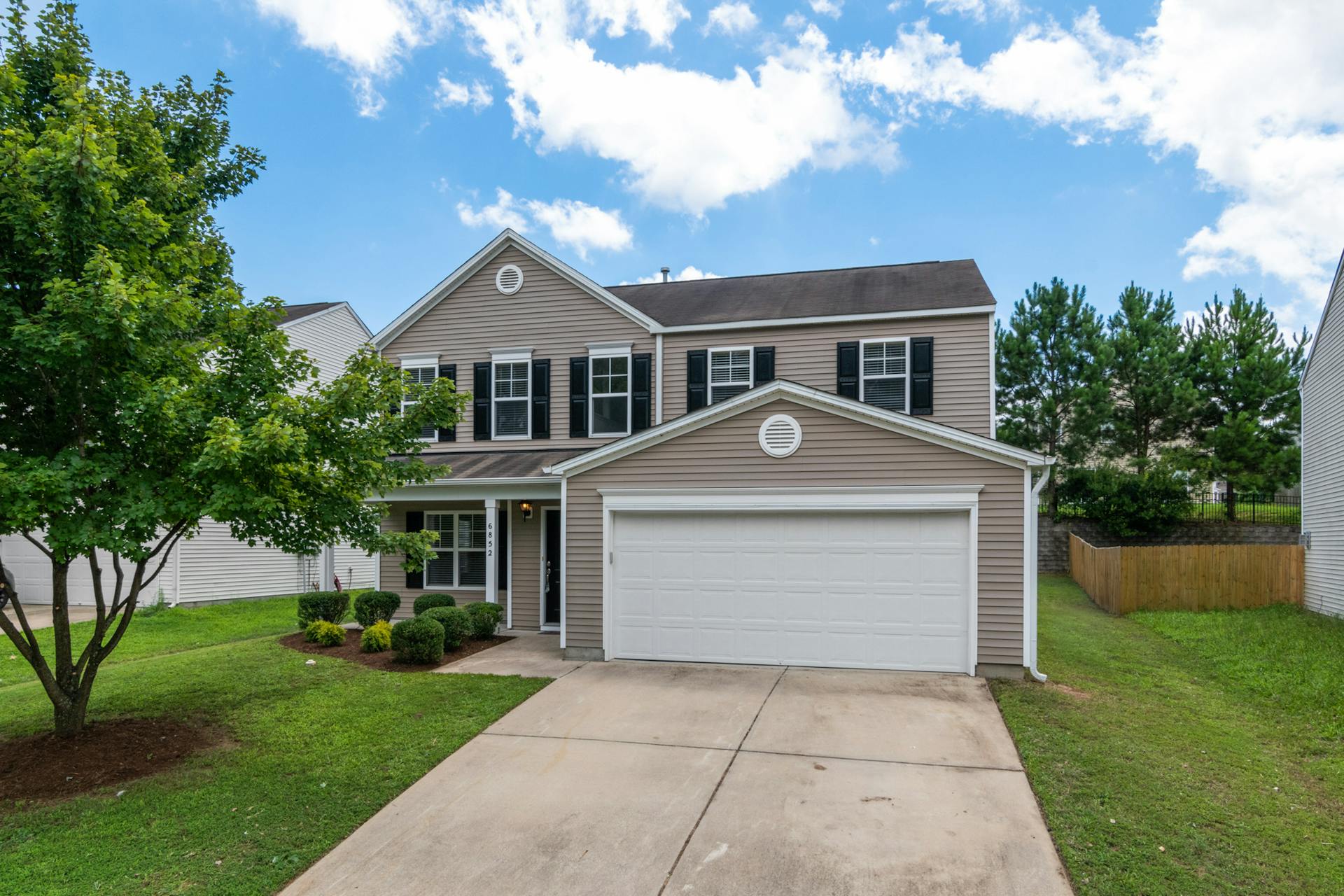 Charming two-story suburban home with green lawn, two-car garage, and blue sky.