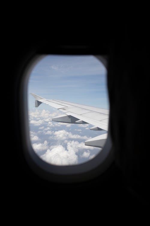 View of Airplane Wing and White Clouds over Blue Sky Out of a Passenger Plane Window