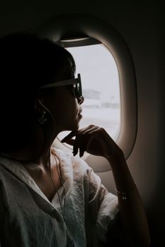 A woman in sunglasses gazes thoughtfully out an airplane window during flight.