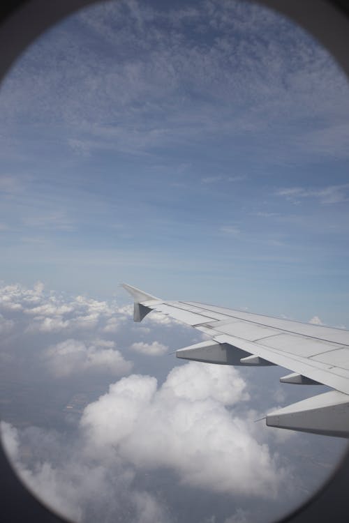 View of Airplane Wing and White Clouds over Blue Sky Out of a Passenger Plane Window