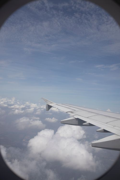 Free View from a plane window showing an airplane wing over fluffy clouds and a clear blue sky. Stock Photo