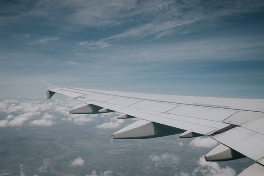 Aerial view from airplane window showing wing and clouds beneath a clear blue sky.