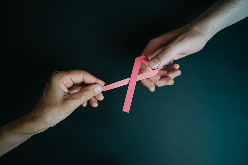 Hands holding pink paper ribbon