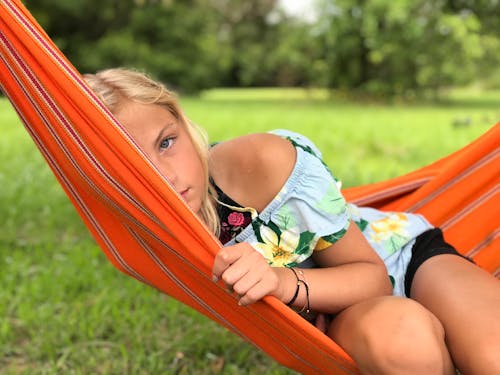 Girl in White and Green Floral Dress Lying on Orange Hammock