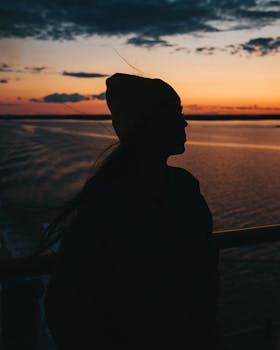 一个女人戴着无檐帽，在水面上观看宁静日落的剪影