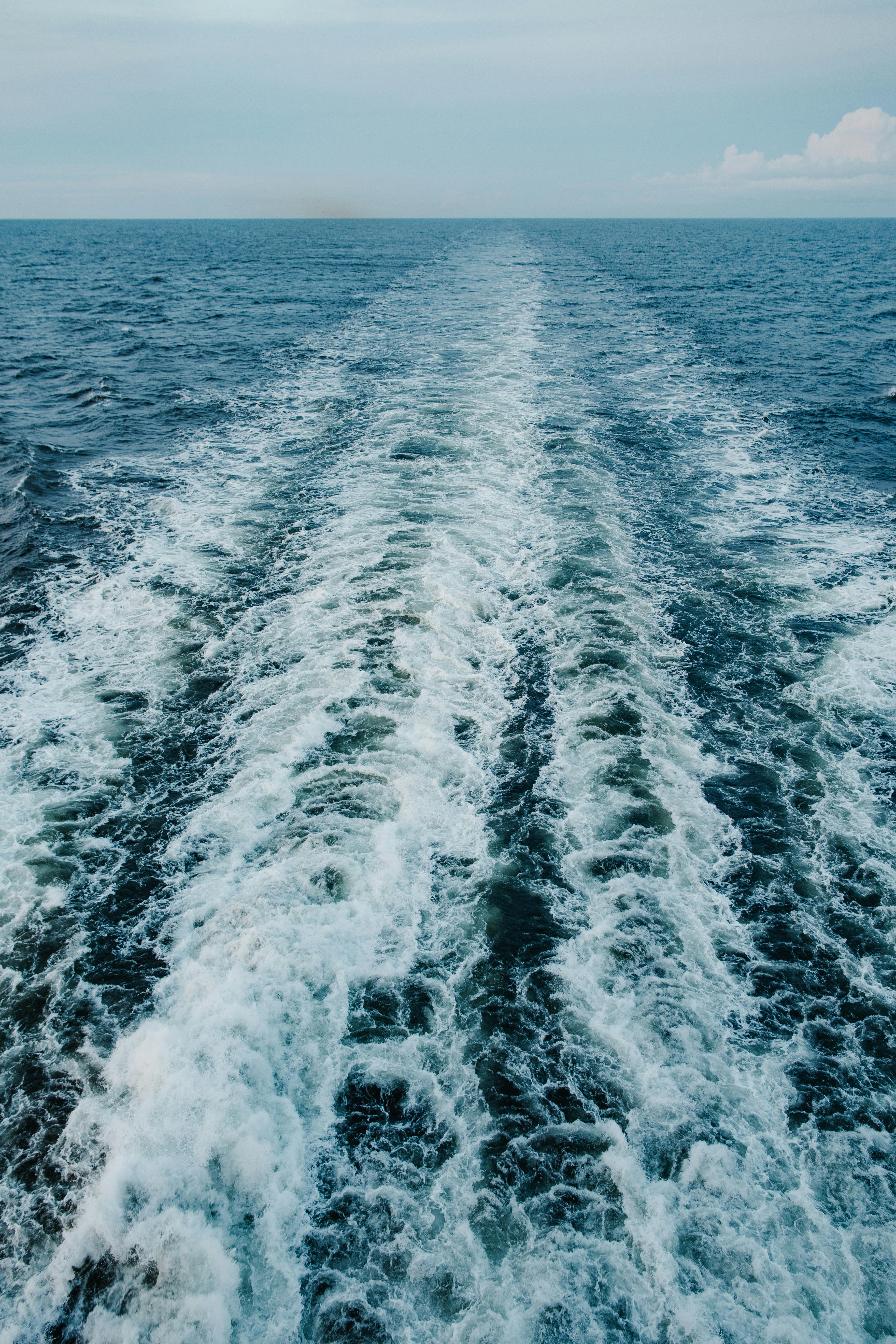 Wake of a boat on blue ocean, with foamy white water trailing behind.
