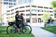 Side view full length serious bicycle patrol policemen in uniforms and helmets standing on city lawn