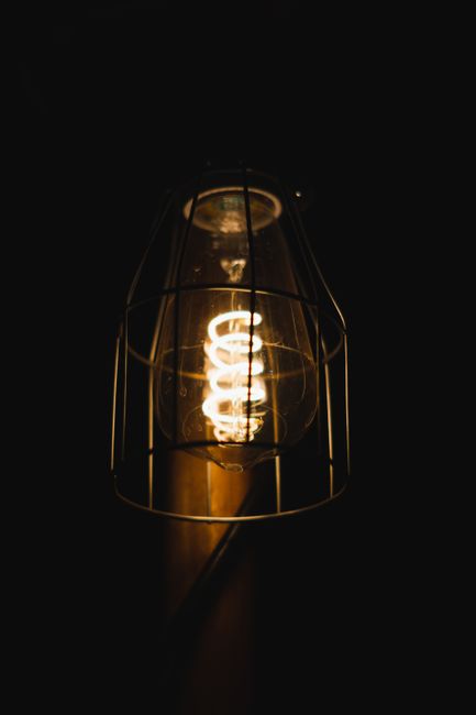 Close-up of a vintage Edison style light bulb with a protective cage glowing warmly against a dark background.