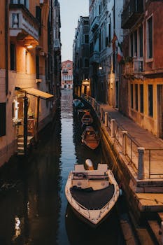 黄昏时分，威尼斯一条狭窄的运河呈现出宁静的景色，展示着标志性的贡多拉和历史建筑