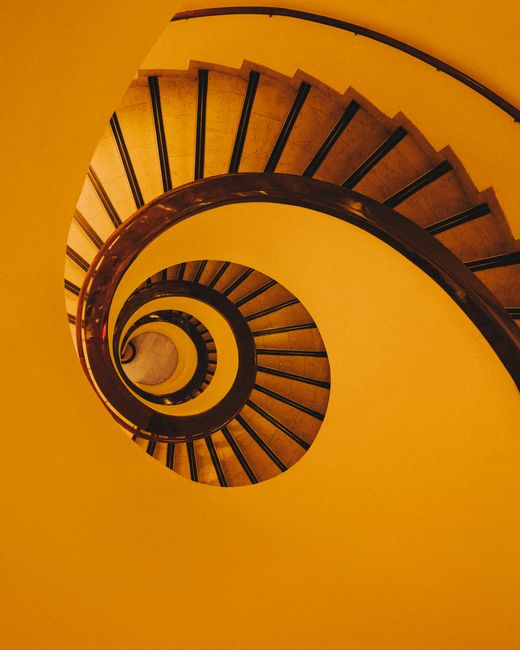 Dramatic spiral staircase viewed from above with a warm, golden tone.