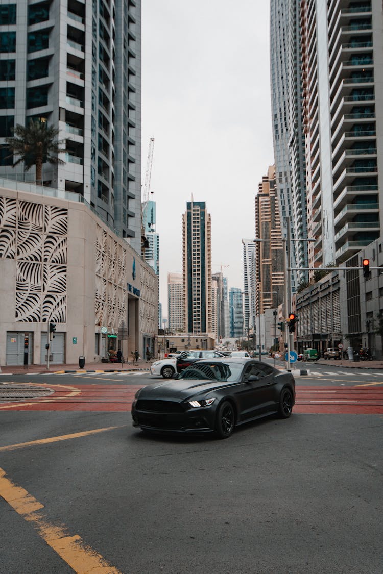 A Black Car On The Road Between Buildings