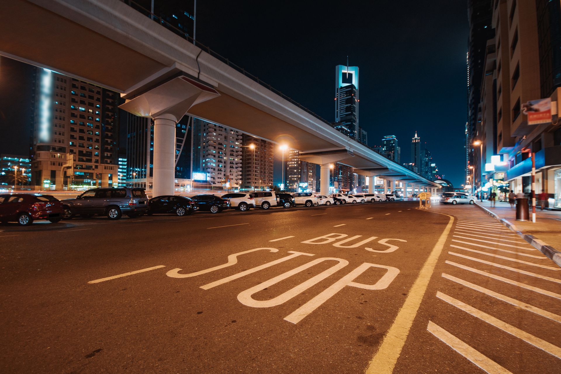 Dynamic nighttime city scene featuring tall illuminated skyscrapers and a marked bus stop.