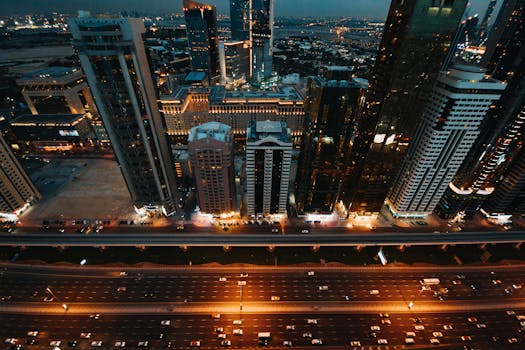 A vibrant urban skyline with illuminated skyscrapers and busy roads captured from above at night.