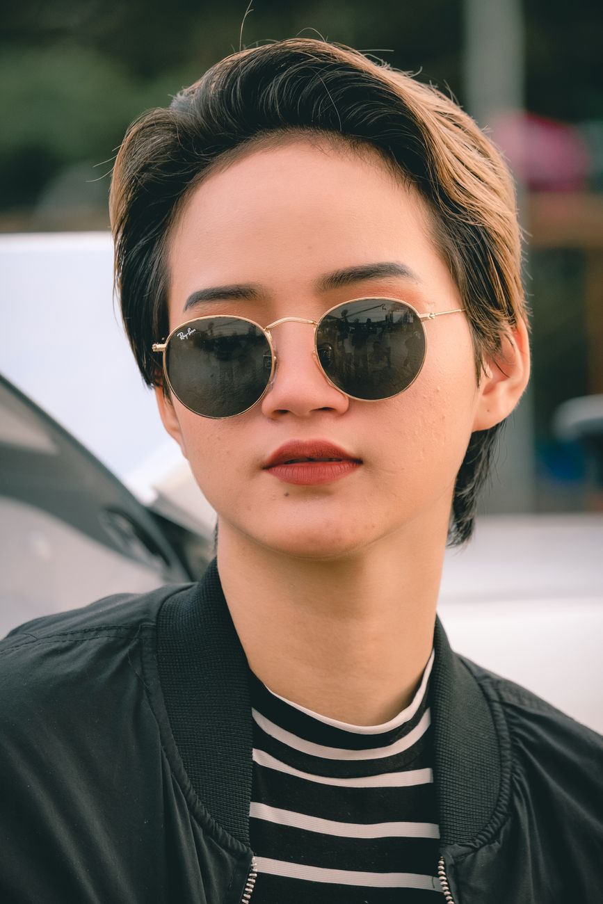 Close-up portrait of a stylish woman with sunglasses and brown hair outdoors.