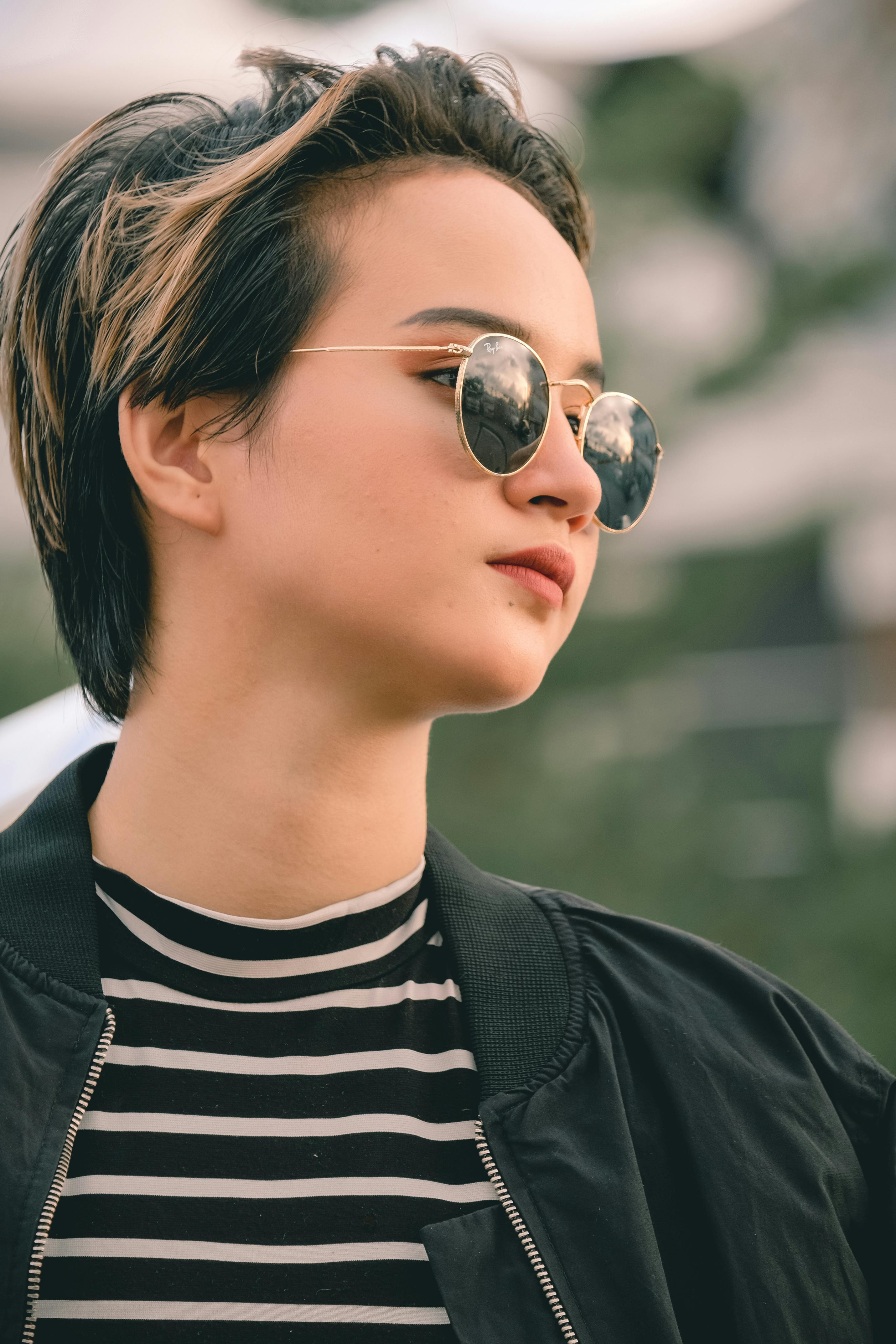 Portrait of a young woman in sunglasses and jacket, with an urban backdrop.