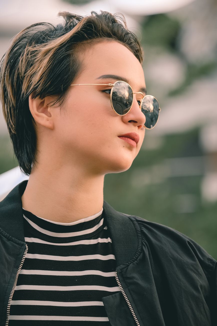 Portrait of a young woman in sunglasses and jacket, with an urban backdrop.