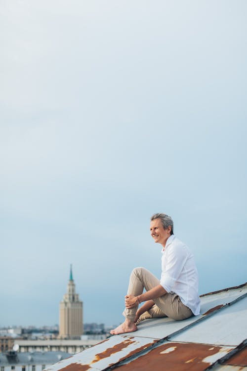 Free Man in White Long Sleeve Shirt Sitting on Roof Stock Photo